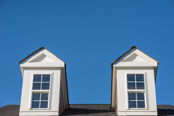 Double white dormer sash window with blue sky background on a gable roof with vinyl siding on a luxury estate house in the East Coast of the USA for upper middle class families