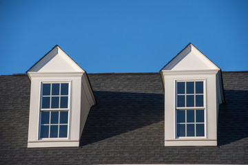 Double white dormer sash window with blue sky background on a gable roof with vinyl siding on a luxury estate house in the East Coast of the USA for upper middle class families