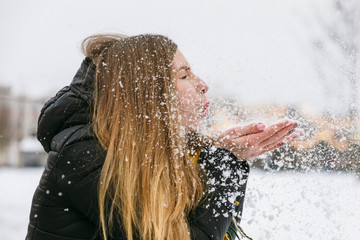 Girl blowing on a handful of snow. Snowfall, winter holidays in February. Give emotions