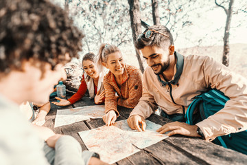 Small group of happy hikers sitting at the table in forest in autumn and looking at map