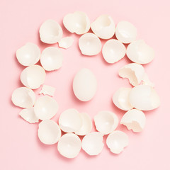 White egg and broken eggs around it on a pink background. The concept of life insurance, health and property, waiting for the birth of a child. Flat lay, top view