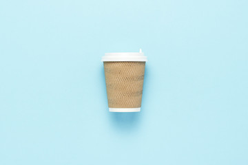 Disposable paper cup with a plastic lid for hot coffee or tea on a blue background. Flat lay, top view
