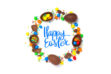 Broken and whole chocolate eggs, multi-colored sweets on a white background. Added text Happy Easter. Circle shape. Concept of celebrating Easter, Easter decorations. Flat lay, top view