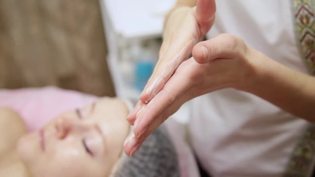 The employee of the spa salon applies an ennobling cream on the face of a young attractive girl close up.