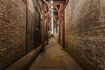 Fototapeta na wymiar Looking down an urban alleyway with brick buildings, steel beams and a string of light bulbs