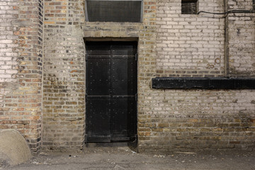 Black metal door against light brown vintage brick building in alleyway
