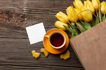 Easter gingerbread cookies, cup of tea on wooden table and yellow tulips. Greeting card. Top view with copy space.