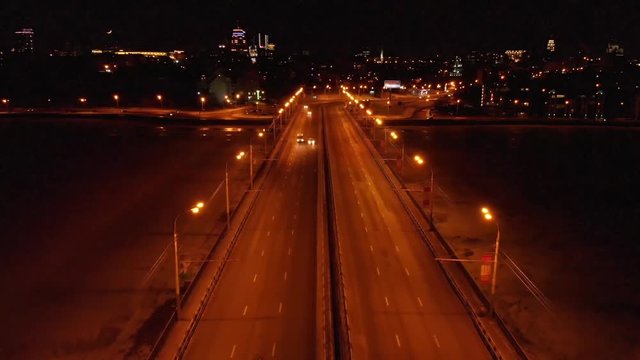 Illuminated bridge with car traffic on night city background, aerial view