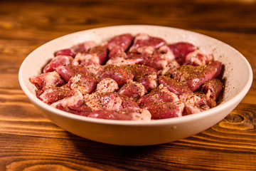 Ceramic plate with raw chicken hearts on wooden table