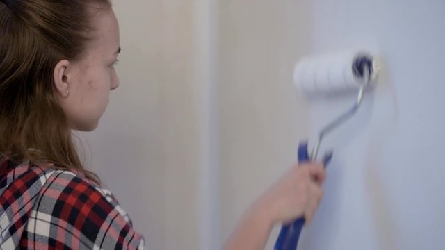 Teen Girl Painting interior Walls at Flat using Paint Roller. Child himself makes Repairs in her room - actively paints wall with white paint. Home renovation or Redecoration concept.