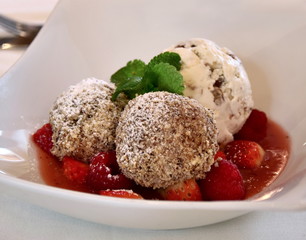 Topfenknödel mit Nougatfüllung, Walnusseis und Waldfrüchte in Fruchtsauce in weißer Schüssel 