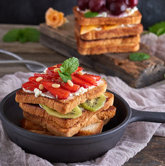 French toast from white bread with cottage cheese, strawberries, kiwi in a black cast-iron round frying pan