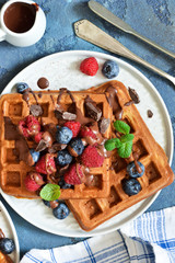 Classic breakfast: waffles with berries and chocolate sauce on a concrete blue background. View from above.
