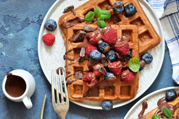 Classic breakfast: waffles with berries and chocolate sauce on a concrete blue background. View from above.