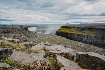 View to river of Dettifoss waterfall and mountains, rocks in the foreground, river is in perspective, Iceland, summer
