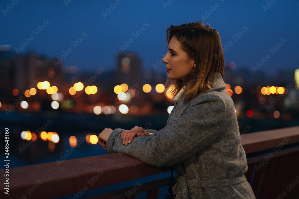 Wall mural woman standing in the ligths of the night city on bridge