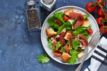 Salad with prosciutto, cherry tomatoes, bread crisps on the kitchen table. View from above.