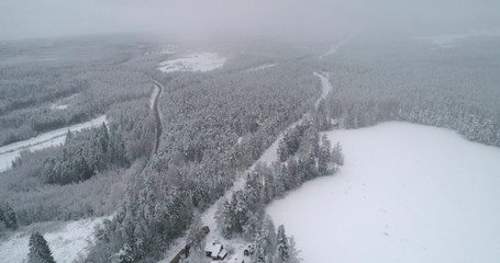 Drone shot, panning around a cargo locomotive, bypassing a pond, in a snowy forest, in nordic countryside, on a overcast, snowstorm, winter, day, in Finland