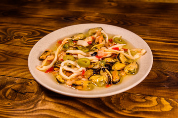 Ceramic plate with different sea food and olives on wooden table