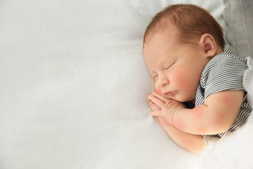 Adorable newborn baby peacefully sleeping on bed, top view with space for text