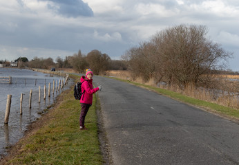 Obraz premium Girl hitchhiking on a rural road wearing a pink coat