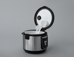 Modern electric multi cooker, parts and accessories on grey background