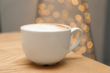 Cup of aromatic cacao on table against blurred lights