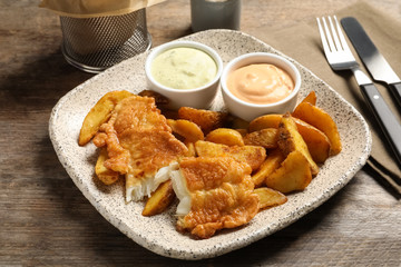 Plate with British traditional fish and potato chips on wooden table