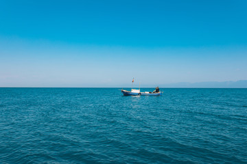 Fototapeta na wymiar Fishermen sitting in a boat while fishing at the sea in the summer season. This fishermen in the wooden boat at the ocean. Fishing under the clean blue sky and seashore