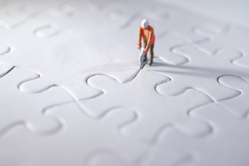 Miniature person constructing puzzles, making way for the team and working concept. Effort concept