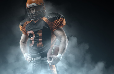 Fototapeta American football player on a dark background in smoke in black and orange equipment. obraz