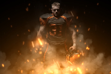 Fototapeta na wymiar American football player on dark background in smoke and sparks in black and orange outfit.
