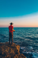 Fisherman standing and throw a fishing rod while fishing at the sea in the summer season. This fisherman on the rocks and seashore. Fishing under the clean blue sky and ocean