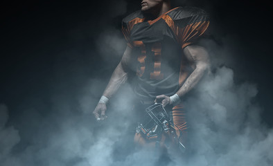 Fototapeta na wymiar American football player on a dark background in smoke in black and orange equipment.
