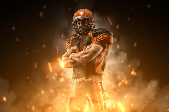 American football player on dark background in smoke and sparks in black and orange outfit.