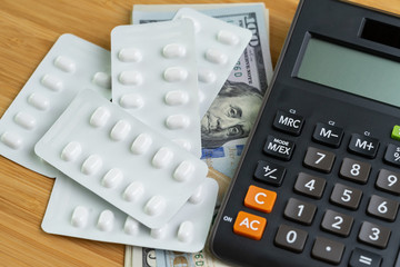 Pills in white package on pile of US Dollar banknotes money with calculator, health care, medical or pharmacy cost concept, patient have to pay for their better life