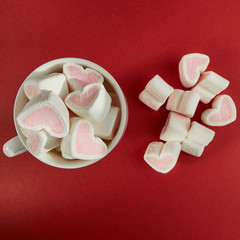 Pink sweet marshmallow hearts in a cup on the red background. Valentine's day background