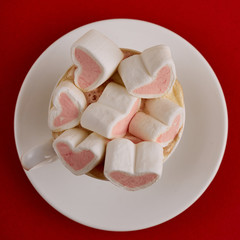 Pink sweet marshmallow hearts in a cup on the red background. Valentine's day background