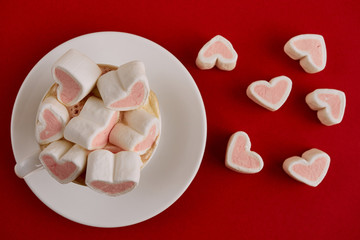 Pink sweet marshmallow hearts in a cup on the red background. Valentine's day background