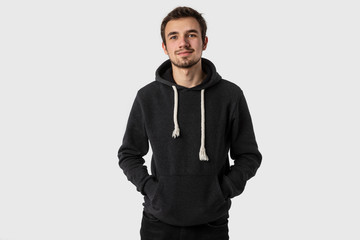 Portrait of satisfied caucasian young man with hands in his hoodie. Isolated on white background.