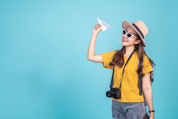 Young Asian woman backpacker traveller holding paper plane over blue background for travel concept