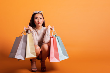 Young beautiful fashionable Asian woman holding shopping bags feel tired and exhausted over orange background studio shot