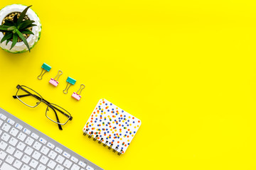Office workplace, work desk in office. Computer keyboard, glasses, stationery, plant on yellow background top view space for text