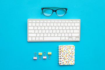Office workplace, work desk in office. Computer keyboard, glasses, stationery on blue background top view copy space