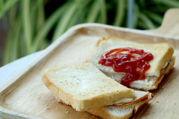 Ham cheese sandwich and tomato ketchup on wood tray and space for write wording, easy delicious food served with coffee or tea in coffee shop or office, popular food for office worker, time saving