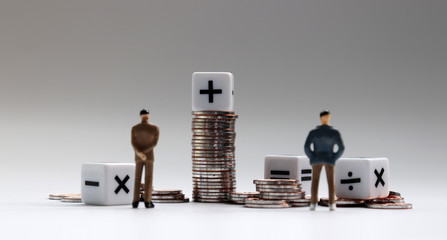 The back of two miniature businessman standing with a pile of coins and arithmetic symbol white...