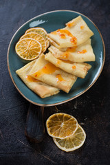 Turquoise plate with crepes, orange sauce and orange fruit chips. Studio shot on a dark brown stone background