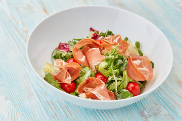 fresh salad with cherry tomatoes and jamon on wooden table
