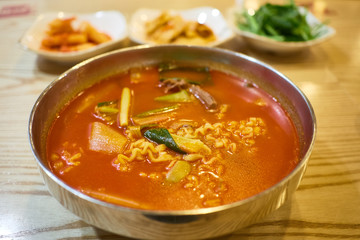 A bowl of kimchi ramen with side dishes in the background