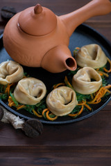 Metal serving tray with steamed asian dumplings and ceramic teapot, vertical shot, closeup